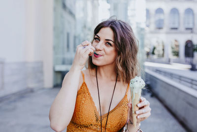 Portrait of woman having ice cream while standing against building in city