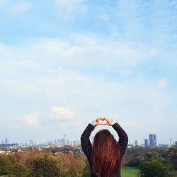 Rear view of woman standing by cityscape against sky