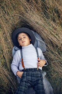 Boy child in plaid pants, hat, suspenders and scarf stands in a field in autumn