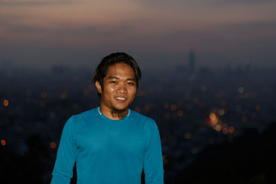 Portrait of smiling young man standing against sky at dusk