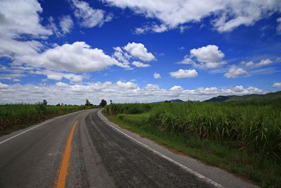 Surface level of road amidst field against sky