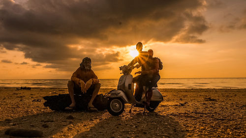 People at beach against sky during sunset