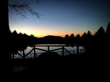 Silhouette trees by lake against clear sky during sunset