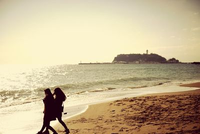 Silhouette people walking on beach against clear sky