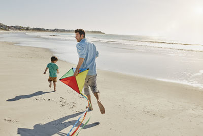 Father and little son playing with kite on the beach