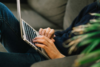 Midsection of man using laptop while reclining on sofa at home