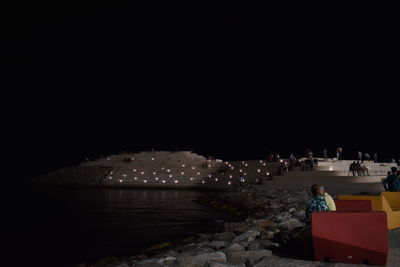 People sitting on illuminated land against clear sky at night