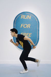 Full length of young man with sign board running against white background