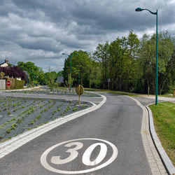 Road sign by trees against sky