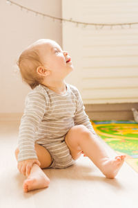 Cute boy looking away while sitting on floor at home