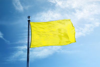 Low angle view of yellow flag against blue sky