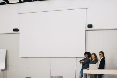 Smiling multi-ethnic technicians standing by blank projection screen at creative office