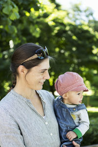 Smiling mother looking away while carrying baby girl outdoors