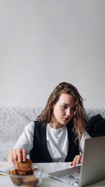 Young woman using laptop while sitting at beach against clear sky