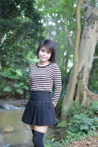 Portrait of smiling young woman standing on field against trees in forest