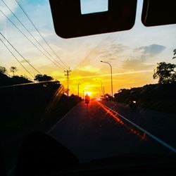 Road amidst silhouette trees against sky seen through car windshield