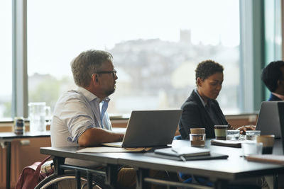 Mature businessman having physical disability sitting on wheelchair with laptop in at meeting in office