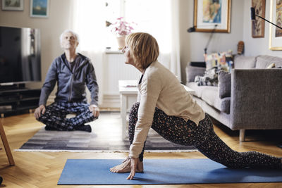 Senior woman and man practicing yoga together in living room at home