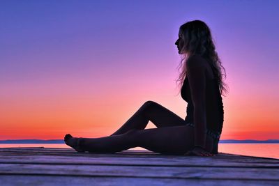 Woman sitting at beach against sky during sunset