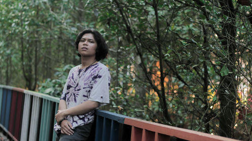 Portrait of man standing by railing against trees outdoors