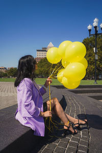 Rear view of woman with yellow balloons against blue sky