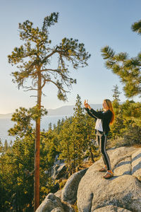 Young woman taking a picture of sunset over lake tahoe.