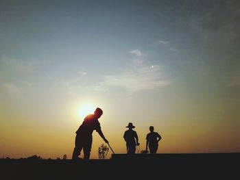 Silhouette people playing soccer against sky during sunset