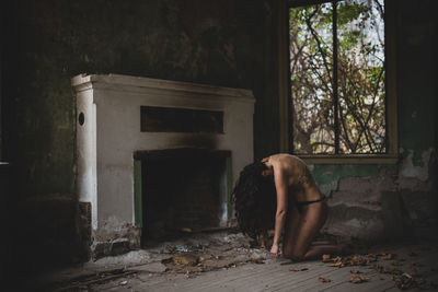 Side view of shirtless woman kneeling in abandoned house