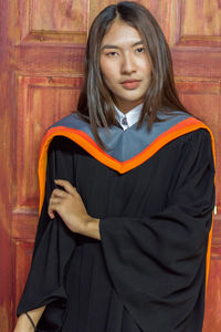 Portrait of beautiful young woman in graduation gown standing door