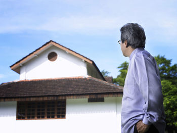 Side view of man standing outside house against sky