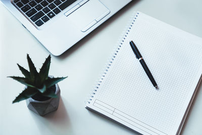 High angle view of modern white office desk table with laptop, pen, notebook and green plants