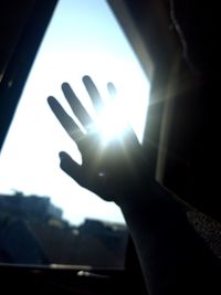 Close-up of human hand against sky seen through window