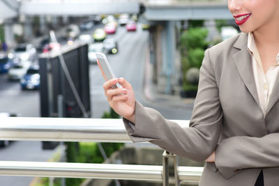 Close-up of businesswoman using phone while standing by railing