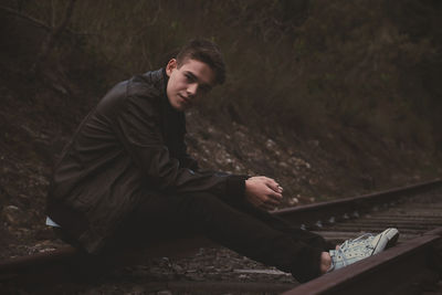 Portrait of teenage boy sitting on railroad tracks