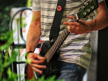 Midsection of man playing guitar outdoors