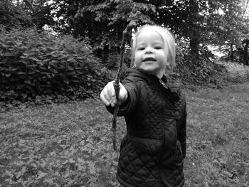 Portrait of girl showing stick while standing on field