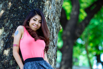 Portrait of young woman standing by tree trunk