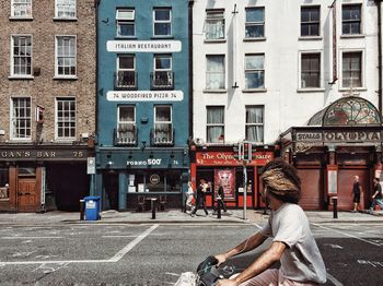 Woman sitting on street against buildings in city