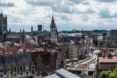 Belfry of ghent by buildings against cloudy sky