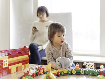 Boy plays with toy blocks. his mother or babysitter texting in smartphone.kindergarten or nursery.