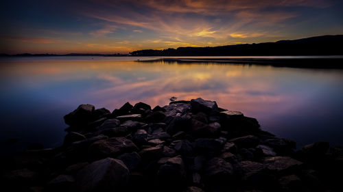 Scenic view of rocks by lake against sky during sunset