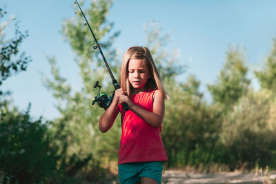 Girl holding fishing rod while walking in forest