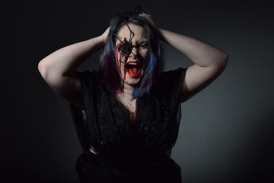 Woman with spider and blood on face screaming against black background