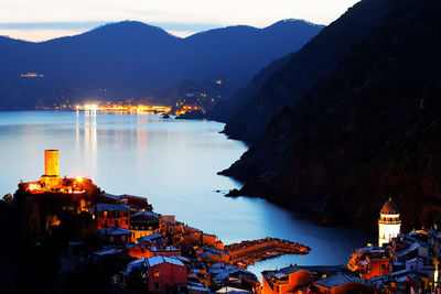 Illuminated village at mountain by sea during sunset