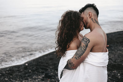 A couple in love spend the night at the sea, kissing and hugging on the beach covered with a blanket