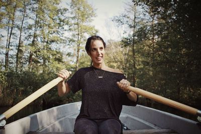 Mid adult woman rowing boat on river in forest