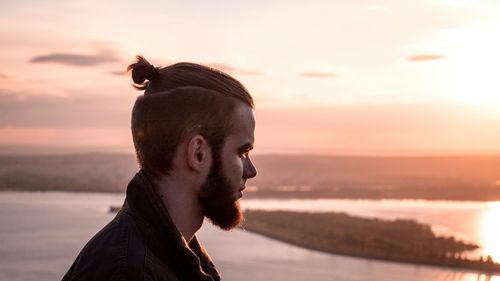 Side view of thoughtful man against sea during sunrise