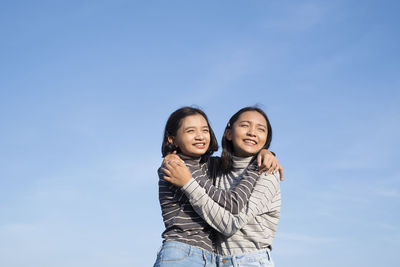 Two young asian girl wear jean and long shirt standing with blue sky.