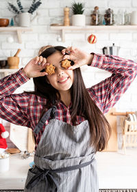 Smiling young woman holding cookie while standing in kitchen