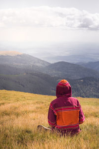 Rear view of person sitting on landscape against mountain range